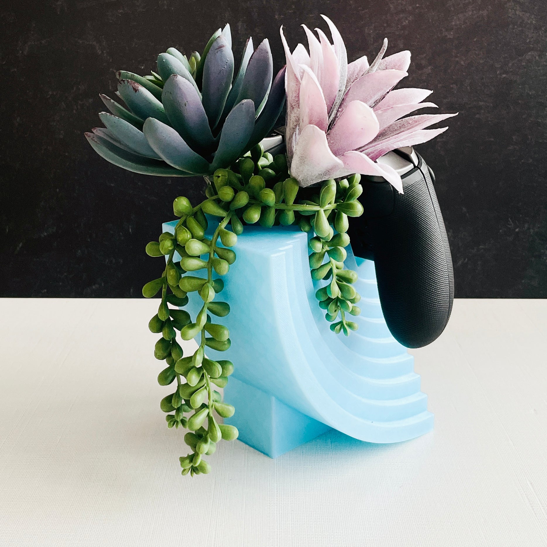 Modern moon 3D printed controller stand holding a generic game controller on desk with faux succulents
