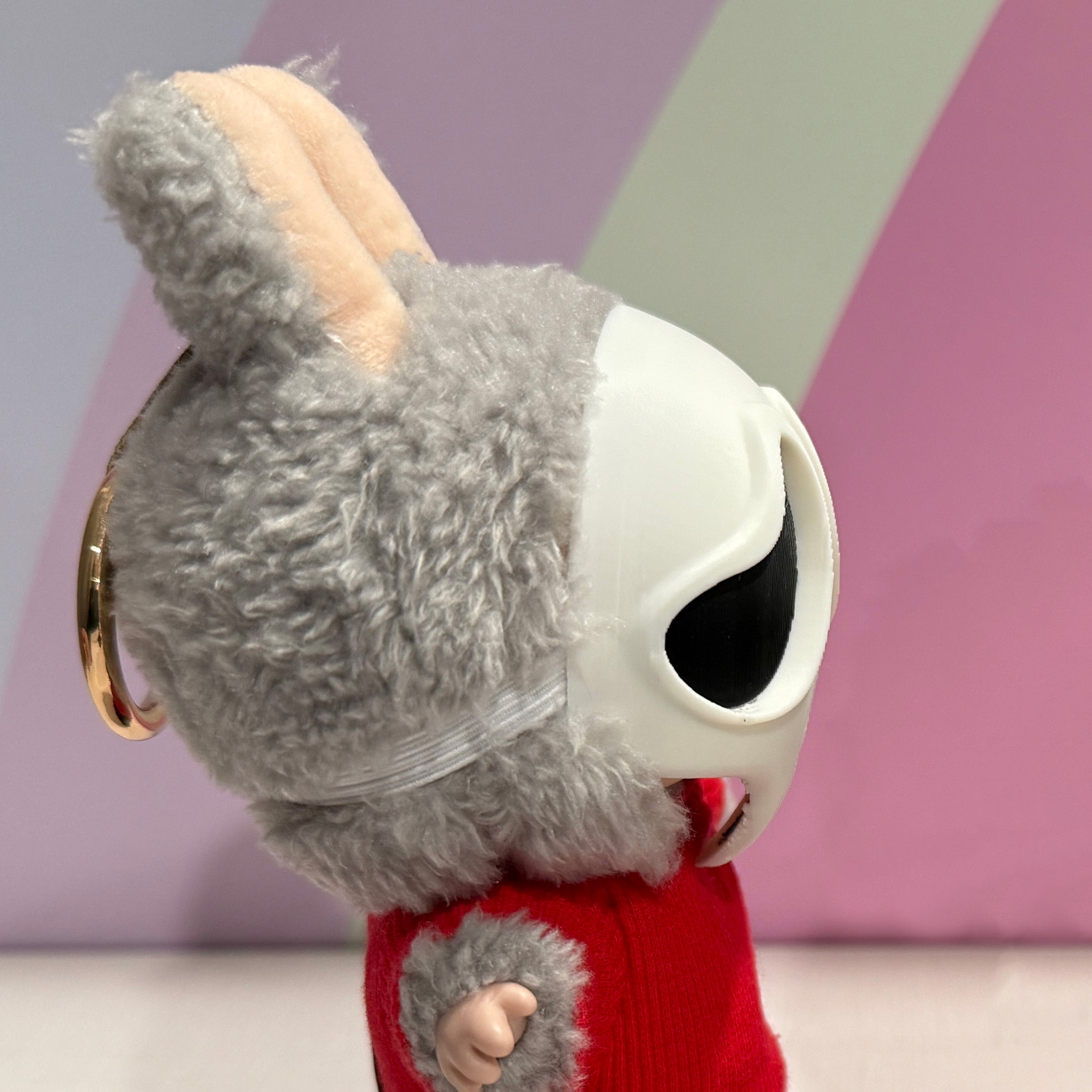 Plush toy with a large white eye and red sweater against a geometric background