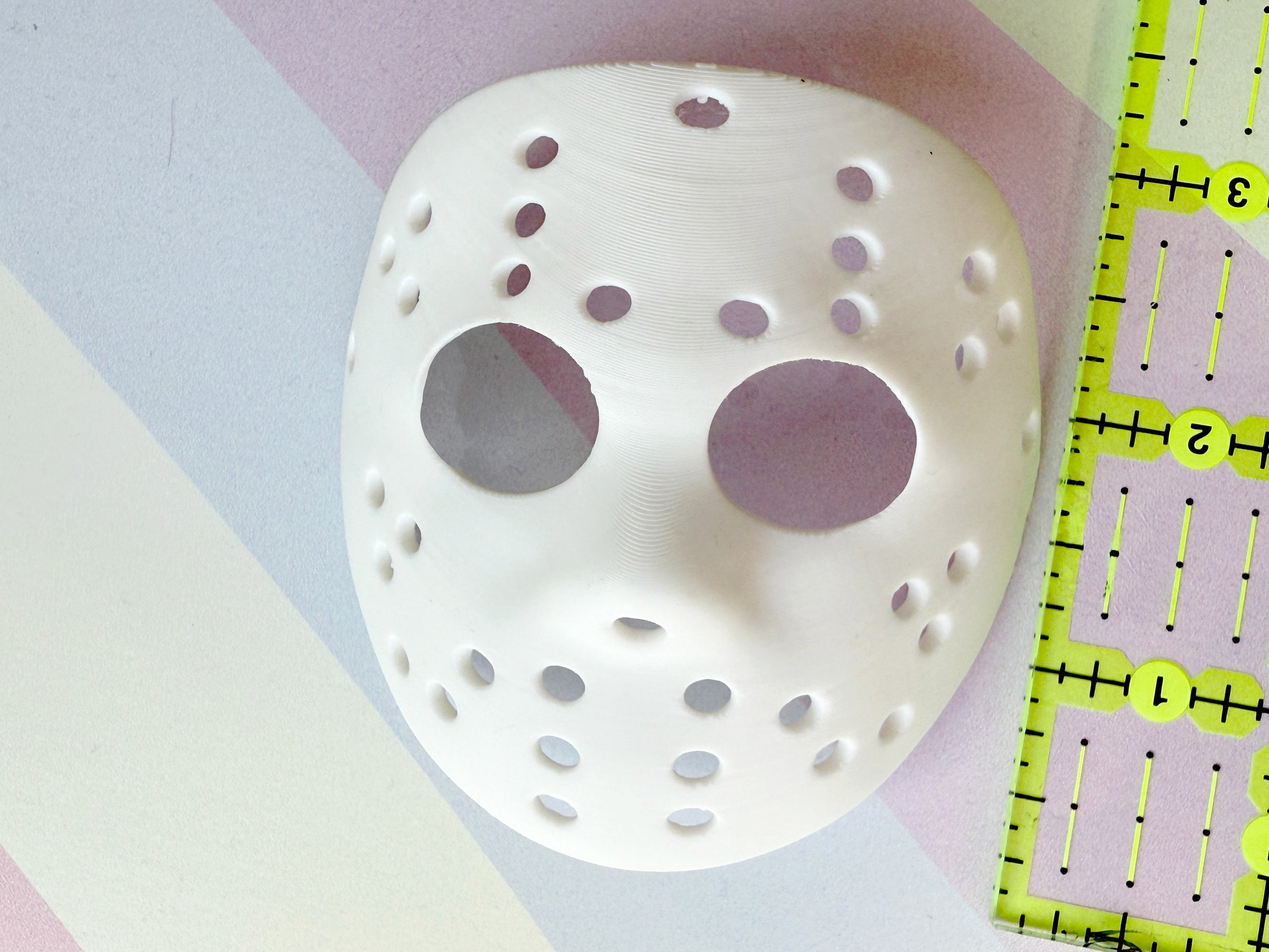 White mask with holes on a colorful background with a ruler for scale