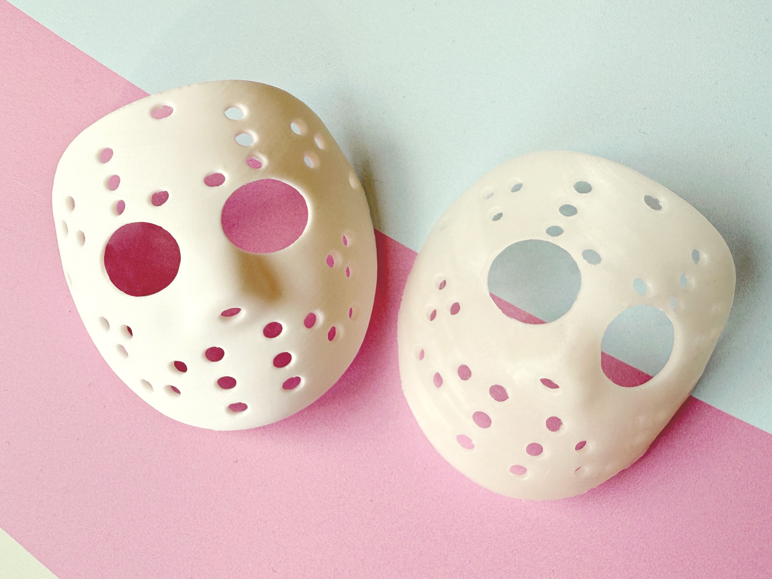 Two hockey masks on a pink and gray background