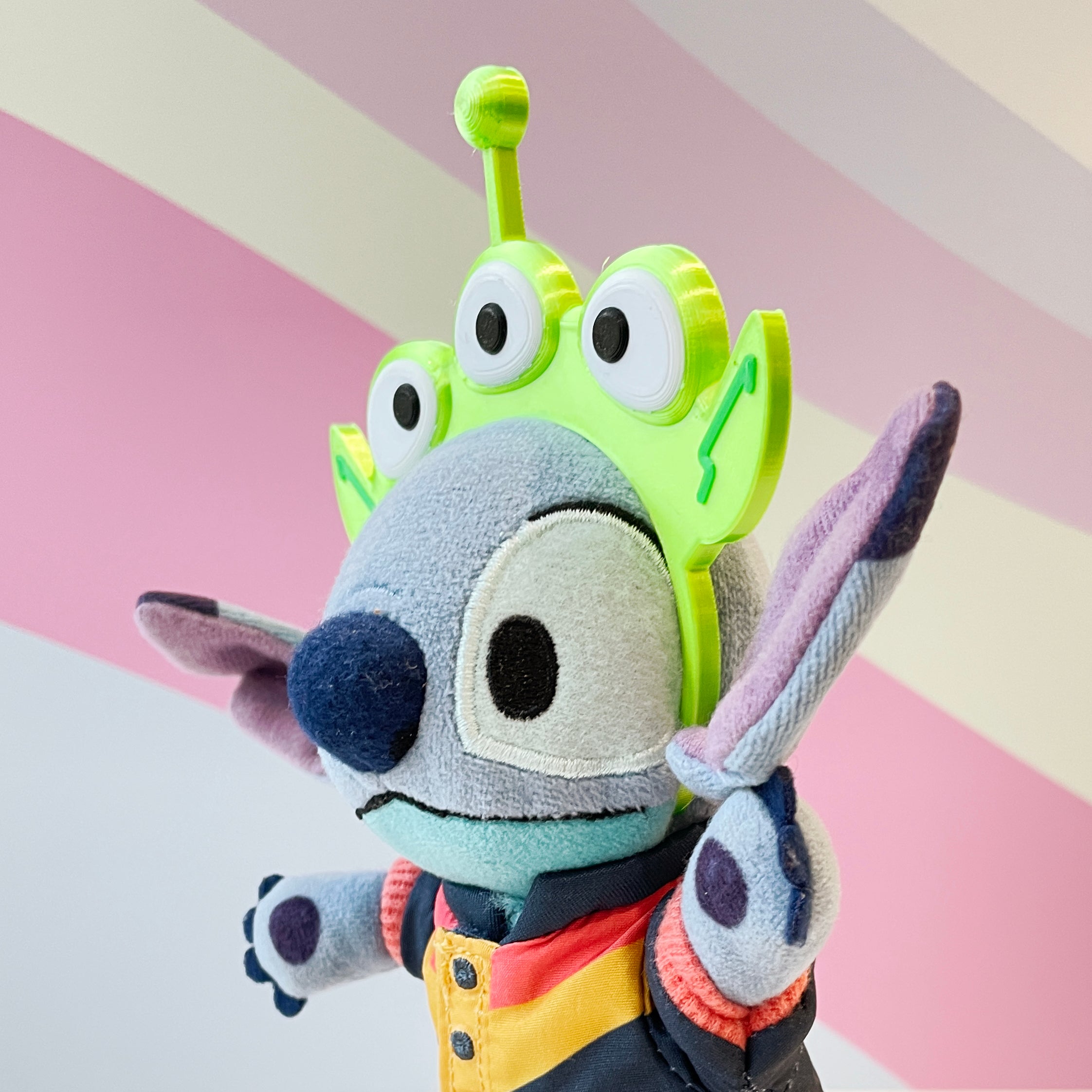 Lime Green Alien Headband with 3 eyes and an antenna on a blue plush on a striped pastel background