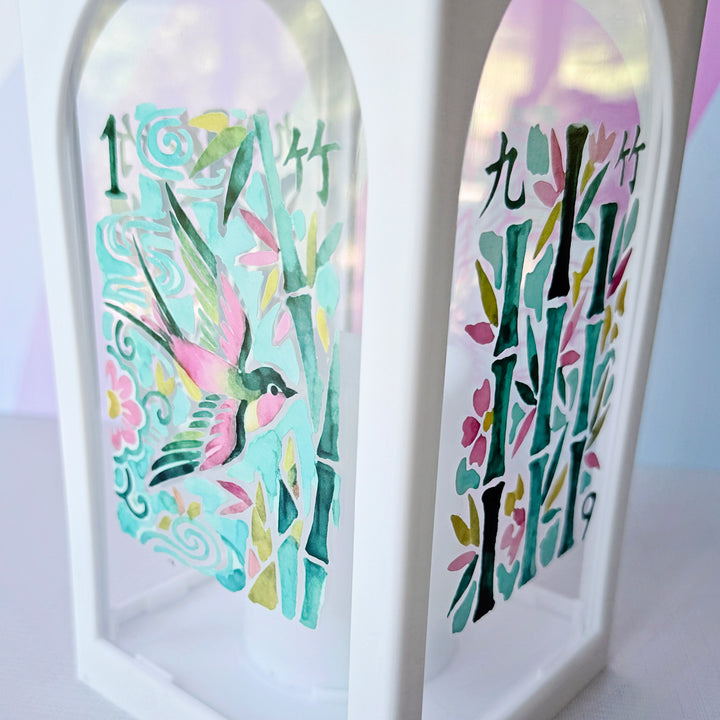 A white decorative lantern with arched side panels, featuring colorful hand-painted bamboo and bird artwork on a soft pastel background.
