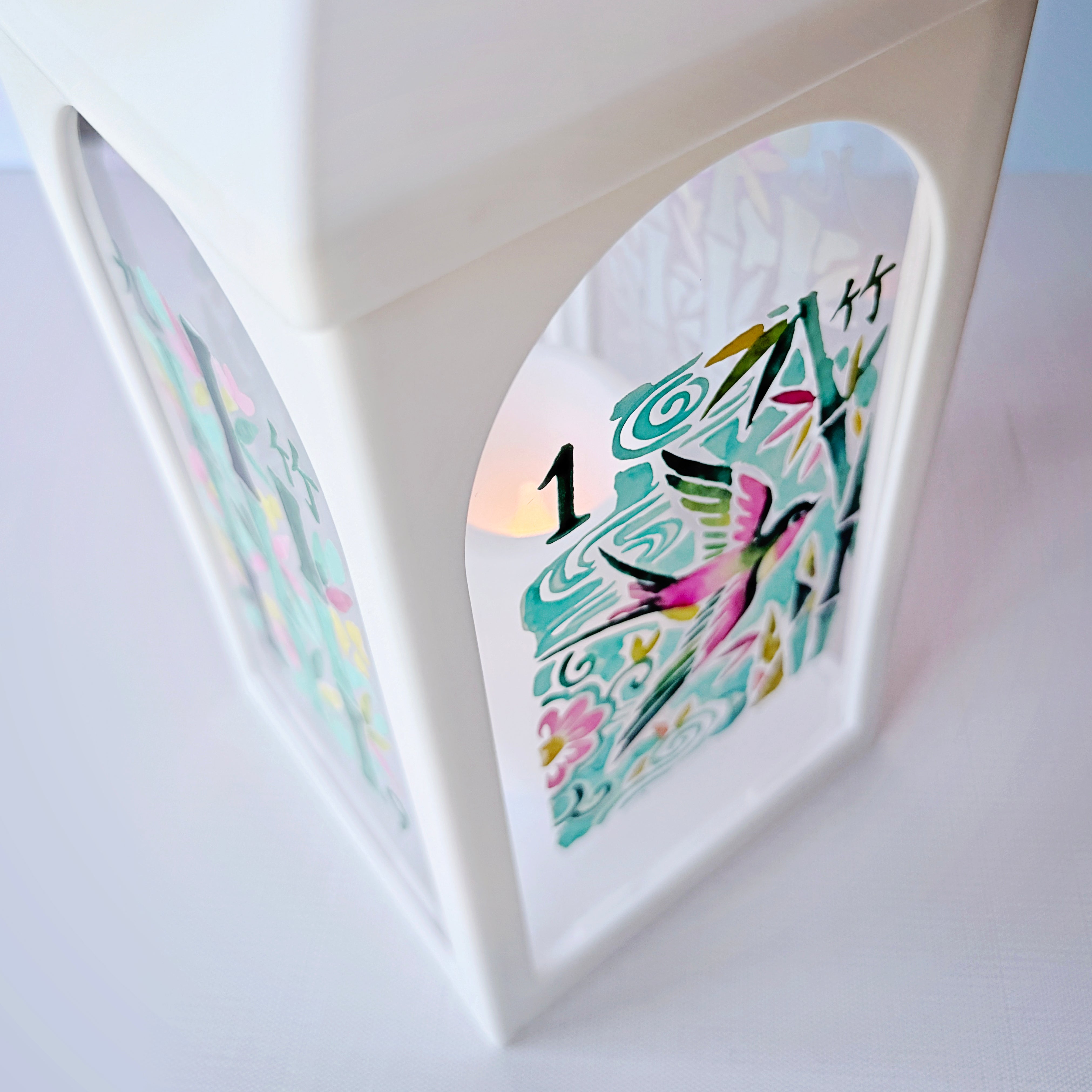 A white decorative lantern with an arched window displaying colorful Japanese-style artwork and the number 1, with a warm light glowing from within.