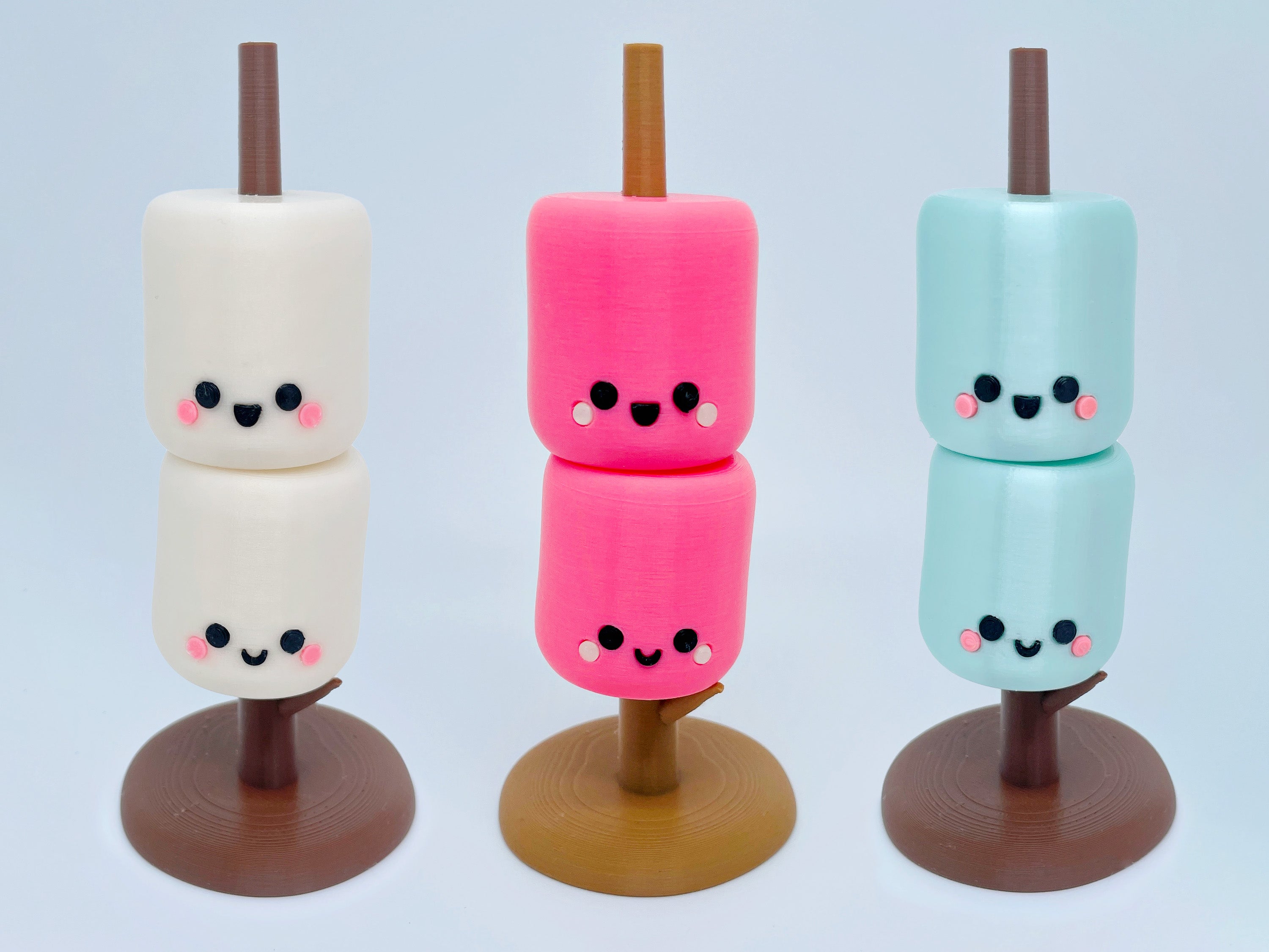 Three marshmallow treats on sticks with cute face designs against a light blue background