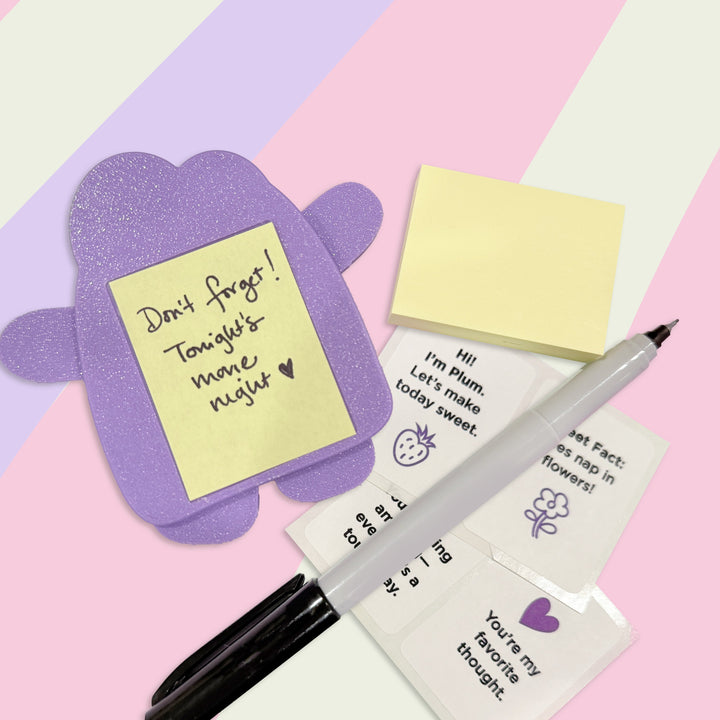 Purple MiNote with note attached to back. Stickers and pen are on a colorful Background