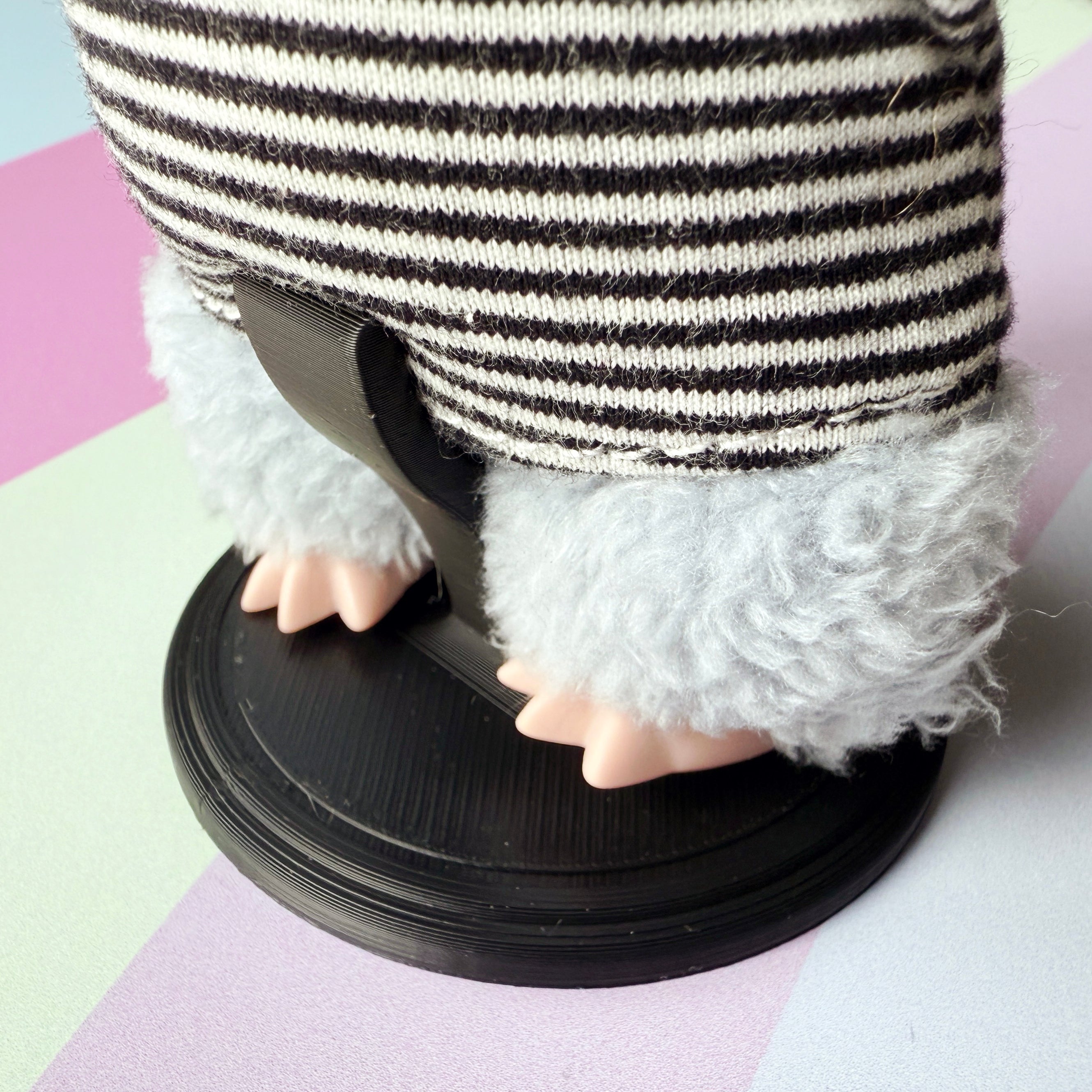 Plush figurine with striped sweater on a black stand against a colorful background