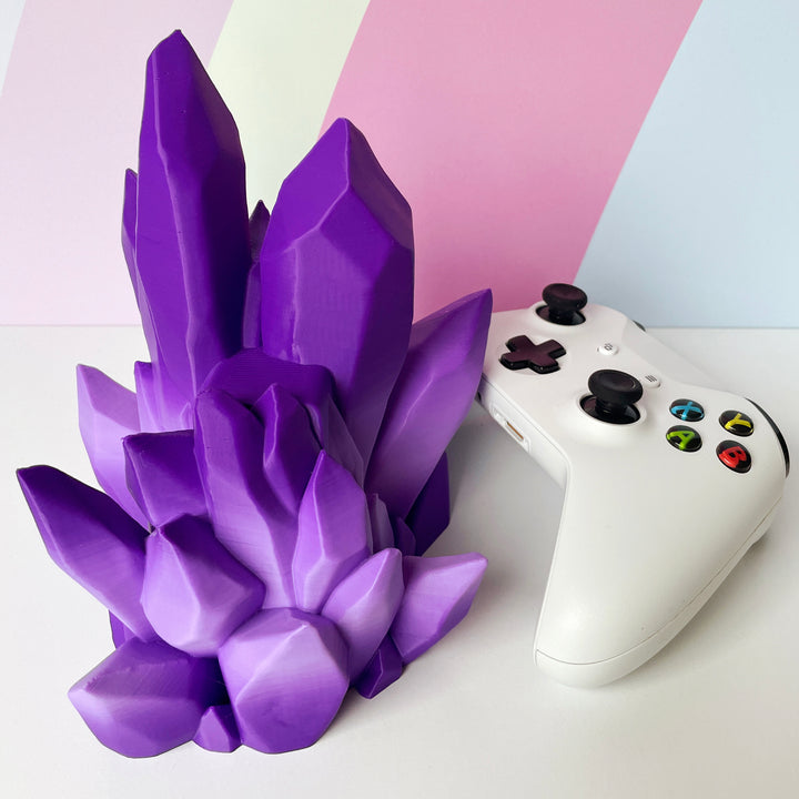 Purple crystal-like object next to a white gaming controller on a light pink and white background